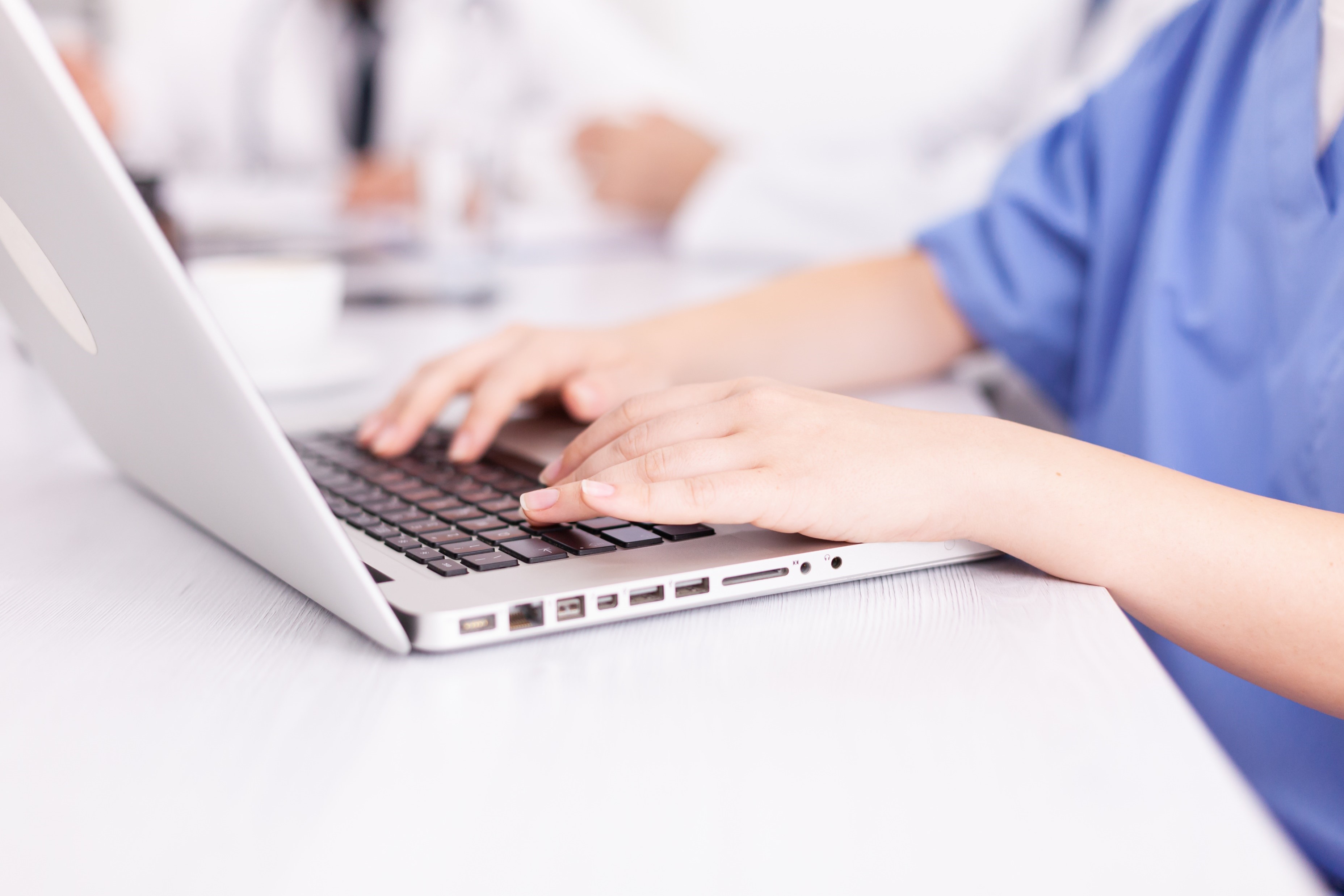 Close-up photo of a nurse typing on a laptop